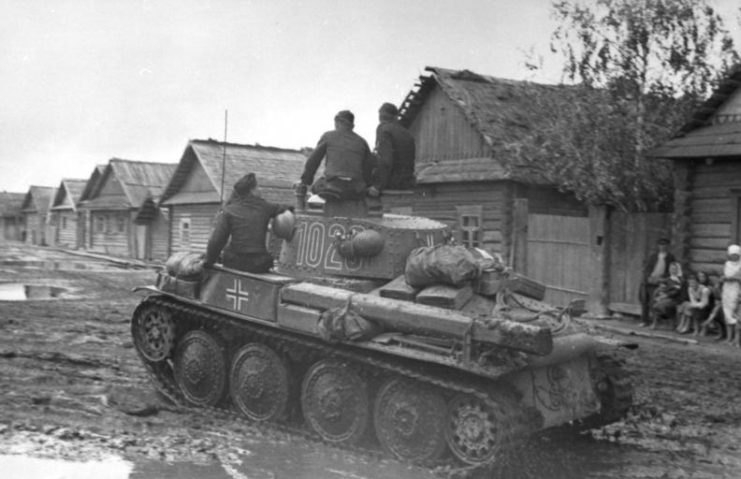 Three soldiers driving a tank through a Soviet town while a family looks on