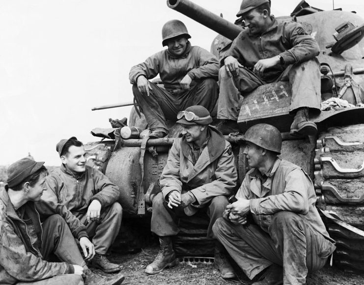 Ernie Pyle and five soldiers sitting on and around a tank