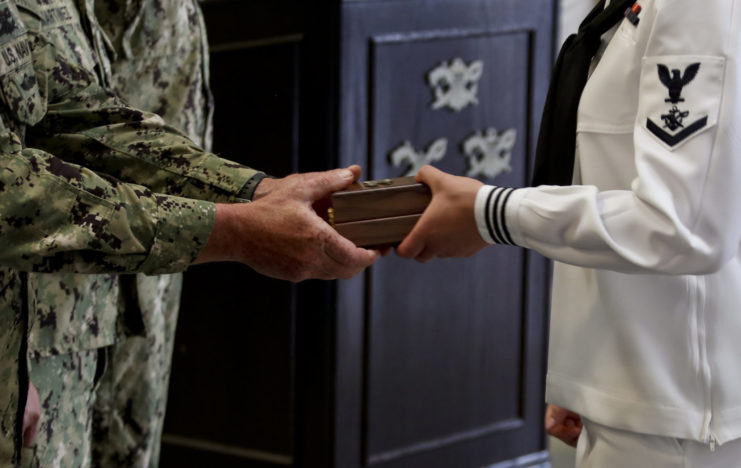 Close-up of a sailor being handed a wooden box by a superior