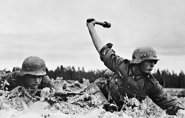 One German troop aiming his rifle while another swings a weapon over his head