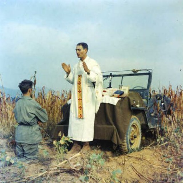 Emil J. Kapaun standing before a kneeling soldier