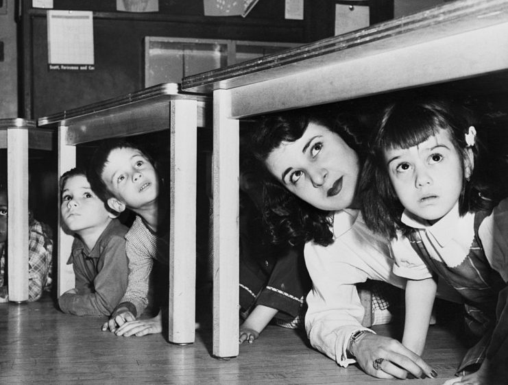Three students and their teacher crouching beneath tables