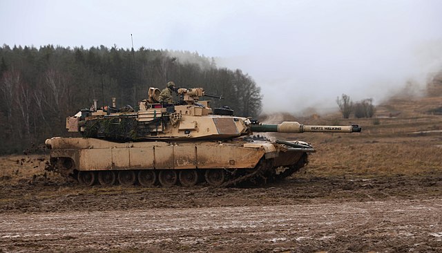 M1A2 Abrams tank being driven across a dirt road