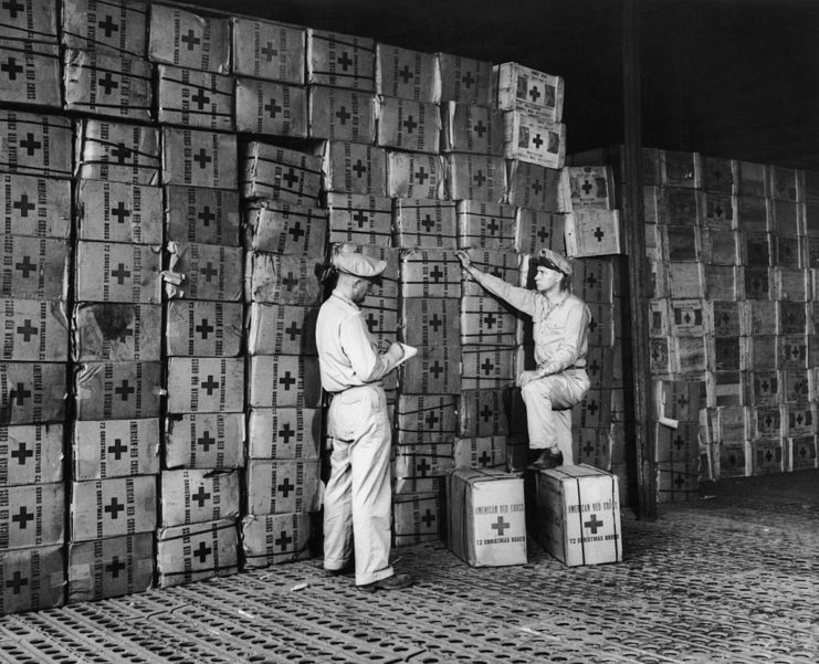 Two American Red Cross workers standing in front of a large pile of packages