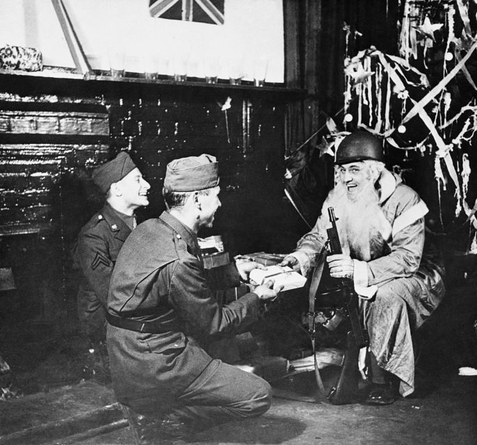 American soldier dressed as Santa Claus handing out presents to two comrades