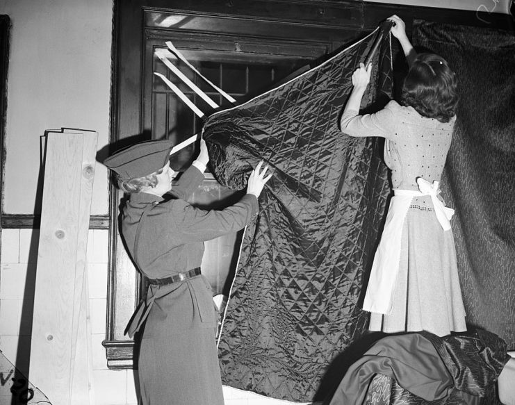 Instructor with the American Women's Voluntary Service teaching a housewife how to hang up blackout curtains