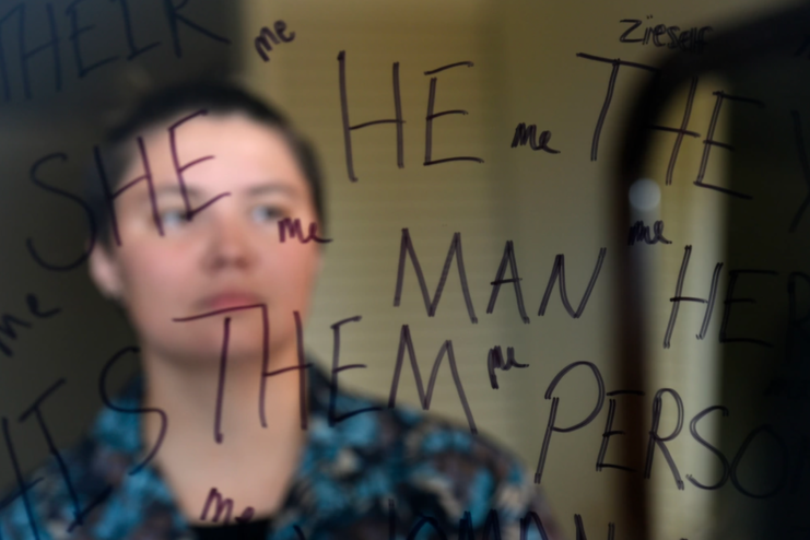 Senior Airman Max Miller looking into a mirror with gender pronouns written on it