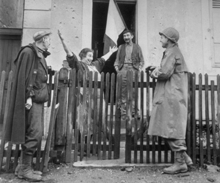 Woman extending her hands in celebration, surrounded by her neighbors and an American soldier