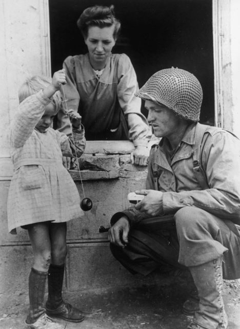 American soldier crouched before a young child holding a yo-yo