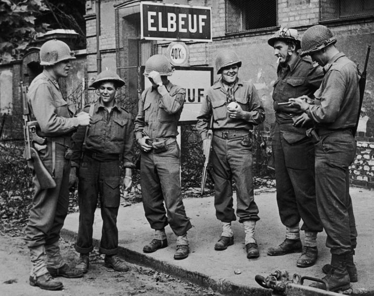 Six US and Canadian soldiers standing around, smoking cigarettes