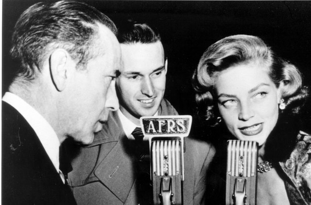 Humphrey Bogart and Lauren Bacall standing in front of microphones with another man