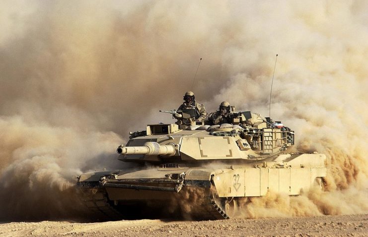 Two soldiers with the US Army 3rd Infantry Division atop an M1/A1 Abrams tank in sandy conditions