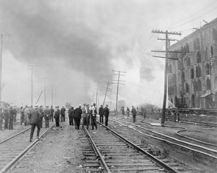 Crowd gathered along railroad tracks covered in smoke