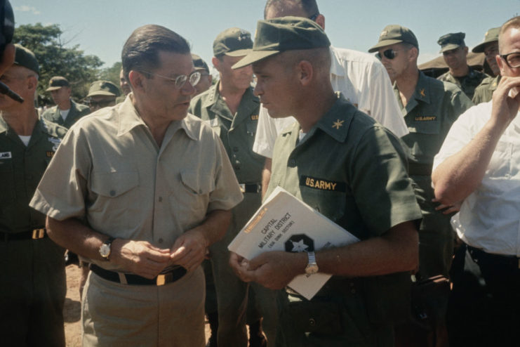 Robert McNamara standing with military personnel