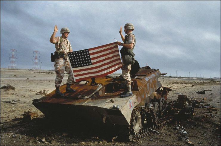 US soldiers saying the oath while holding the American flag atop a burnt Iraqi tank