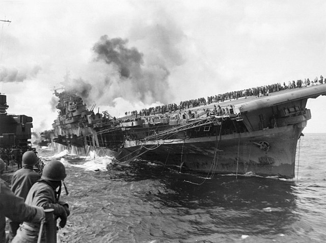 Crew of the USS Santa Fe watching a smoking USS Franklin list in the water