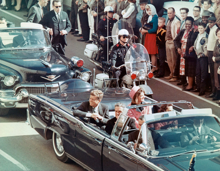 John F. Kennedy and Jacqueline Kennedy riding in a convertible driving by lines of people