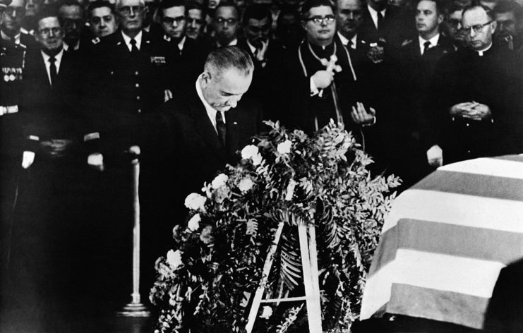 Lyndon B. Johnson praying before the foot of John F. Kennedy's flag-draped coffin