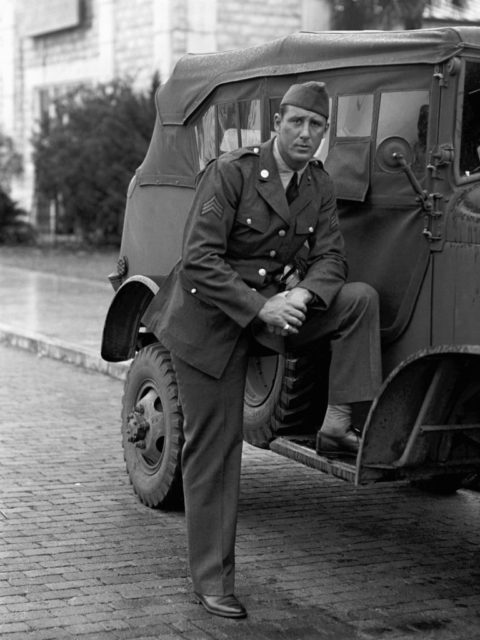 Hank Greenberg posing next to a Jeep