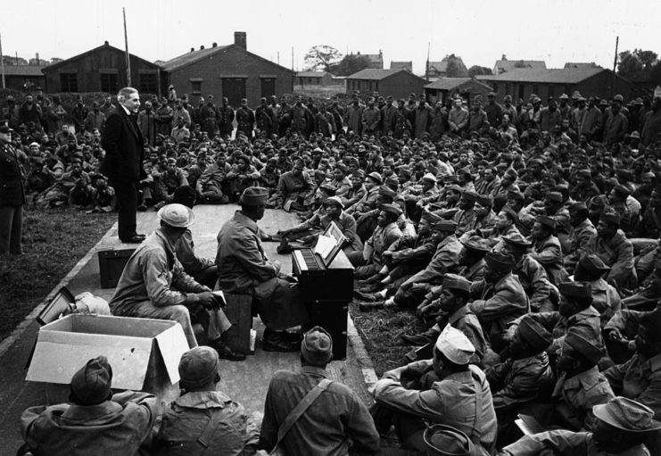 African-American soldiers gathered around an Army chaplain playing the piano