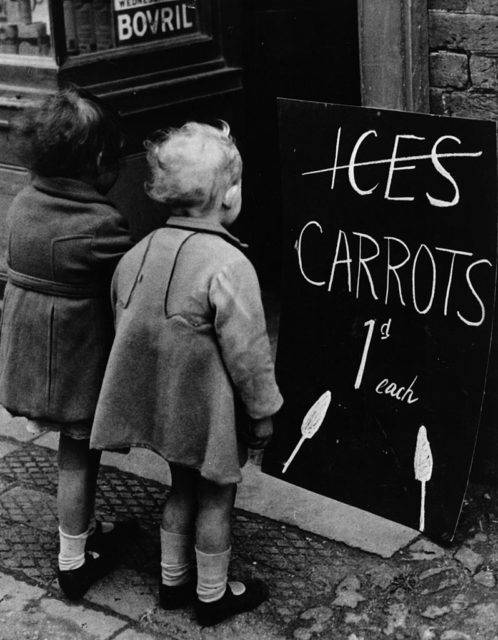 Two girls looking at a sign for carrot lollies 1941