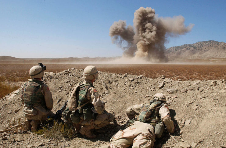 Three soldiers watch as a cloud of smoke rises following a C-4 explosion.