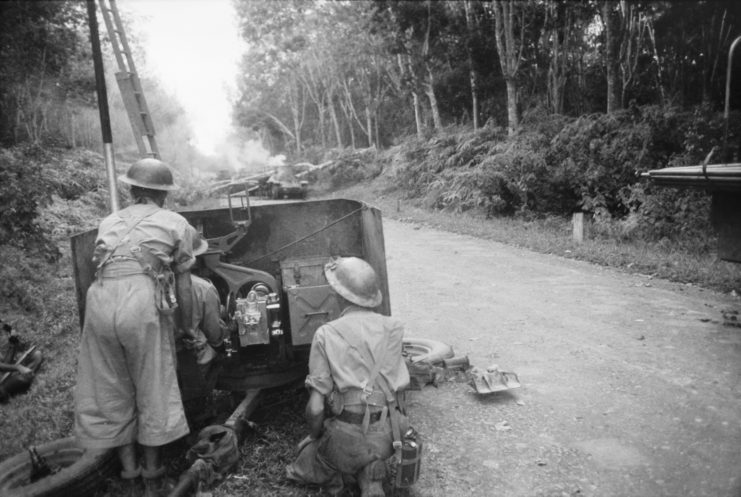 Two Australian soldiers man a tank on a dirt road in Malaya.