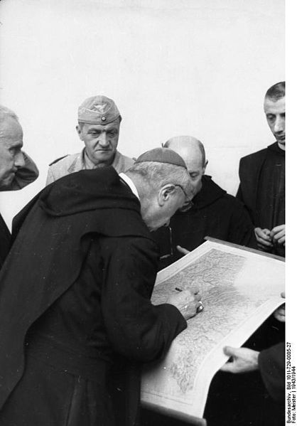 Montecassino Abbey, Italy, 1943. Bishop Gregorio Vito Diamare, Abbot of Montecassino Abbey looks at a map during the packing of artworks from the Abbey about to be transferred to more secure places. The transfer was organized by the German Oberstleutnant (Lieutenant Colonel) Julius Schlegel (a roman catholic from Wien), Division "Hermann Göring" (background, in field uniform).