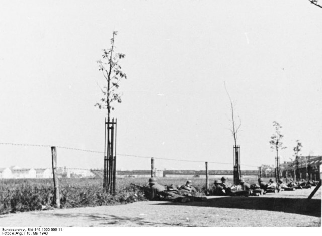 German troops take cover on road parallel to the Maas river. In the background a destroyed bridge can bee seen. It was demolished by the Dutch army to deny it's use to the Germans