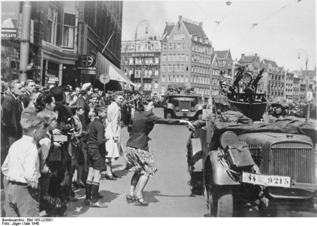 Victorious German troops enter Amsterdam. Most onlookers stare in silence, a handful greets the occupiers. By Bundesarchiv – CC BY-SA 3.0 de