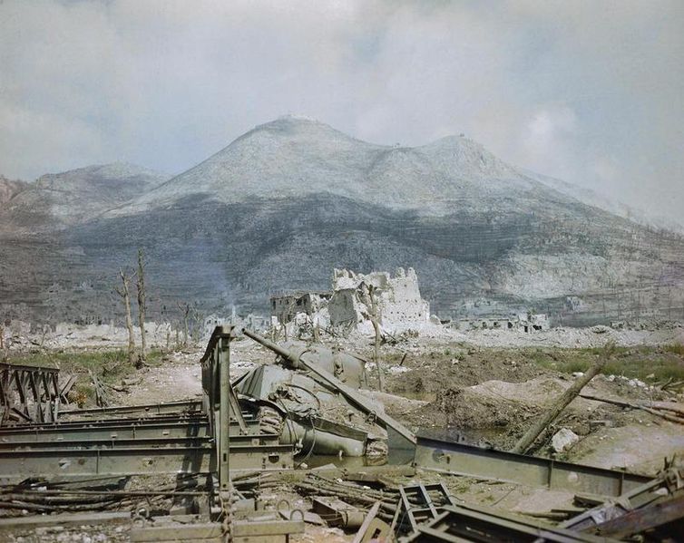The_ruins_of_Cassino,_May_1944-_a_wrecked_Sherman_tank_and_Bailey_bridge_in_the_foreground,_with_Monastery_Ridge_and_Castle_Hill_in_the_background._TR1799