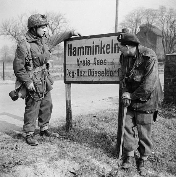 595px-British_airborne_troops_study_a_sign_outside_Hamminkeln_during_operations_east_of_the_Rhine,_25_March_1945._BU2292