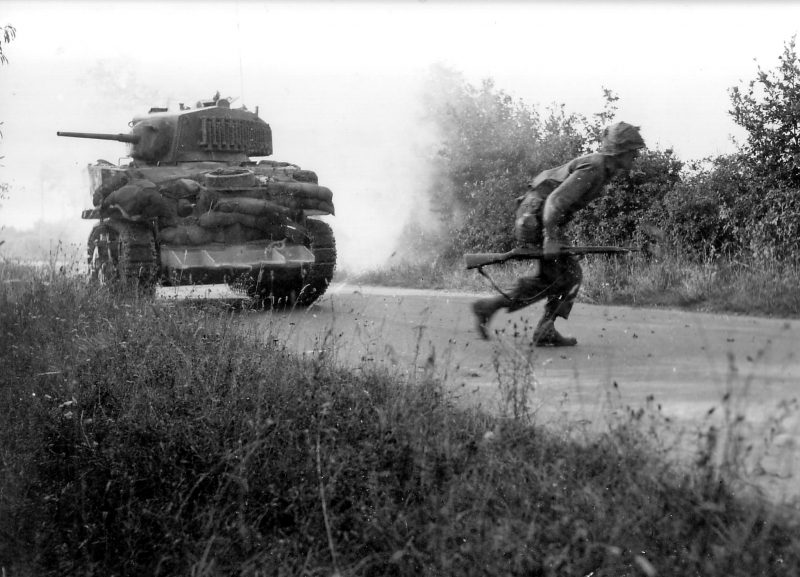 American Soldier crosses the road, covered by an M5A1 stuart tank, note the hedgerow clipping device on the front of the tank.