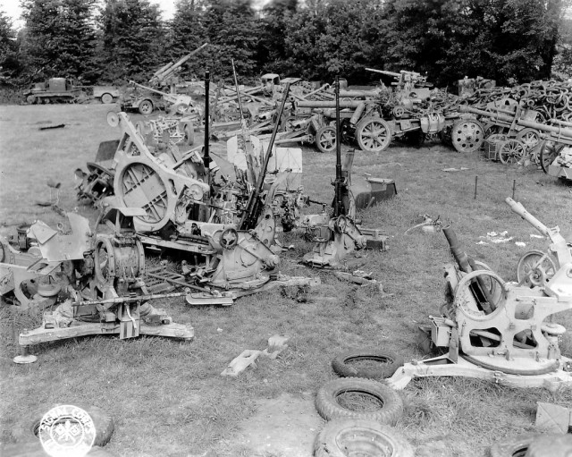 Photo prise dans un dépôt US près d'Isigny-sur-Mer. Après le croissement de la D196 et la D203 en direction de Lison, à l'est du Hameau de la Madeleine. http://www.flickr.com/photos/mlq/5776184661/in/photostream On peut reconnaître : Des pièces d'artillerie allemande sabotées avant le repli des forces du Reich. Au fond " en central " deux canons de 88mm que l'on retrouve sur le p012032 La même pièce et les piquets: Voir ici: http://www.flickr.com/photos/mlq/1341108925/ Reportage de 6 photos sur ce parc de matériel allemand : 4 repérées : p012031, p012032, p013086 et p013441. Et deux, sous réserve : p012028 et p.012034. http://www.flickr.com/photos/mlq/5786951602/in/photostream