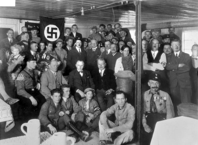 Hitler with Nazi Party members in 1930. By Bundesarchiv – CC BY-SA 3.0 de