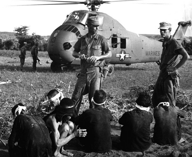 Viet Cong prisoners under guard by US Marines on 1 August 1965 south of Chu Lai. In the background is a Sikorsky UH-34D Seahorse helicopter
