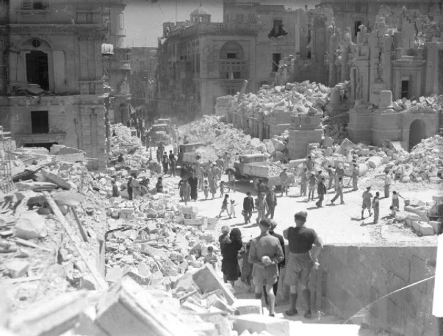 Service personnel and civilians clear up debris on a heavily bomb-damaged street in Valletta, Malta on 1 May 1942