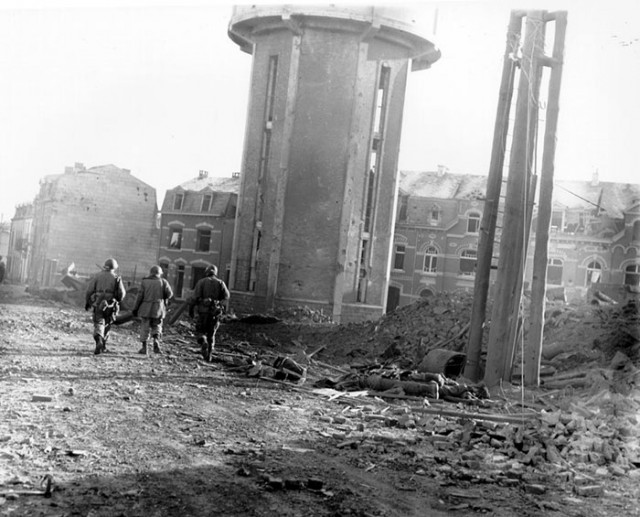 Members of the 101st Airborne Division walk past dead comrades, killed during the Christmas Eve bombing of Bastogne, Belgium, the town in which this division was besieged for ten days. This photo was taken on Christmas Day. 1944 