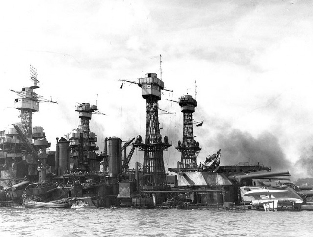 The sunken battleship USS West Virginia (BB-48) at Pearl Harbor after her fires were out, possibly on 8 December 1941. USS Tennessee (BB-43) is inboard. A Vought OS2U Kingfisher floatplane (marked "4-O-3") is upside down on West Virginia's main deck. A second OS2U is partially burned out atop the Turret No. 3 catapult. Note the CXAM radar antenna atop West Virginia´s foremast. 