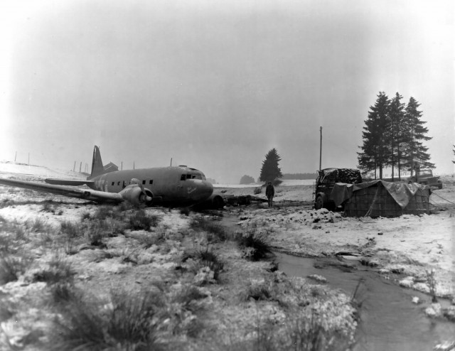 US Army soldier standing next to a C-47 Skytrain wreck, near Bastogne, Belgium, circa early 1945