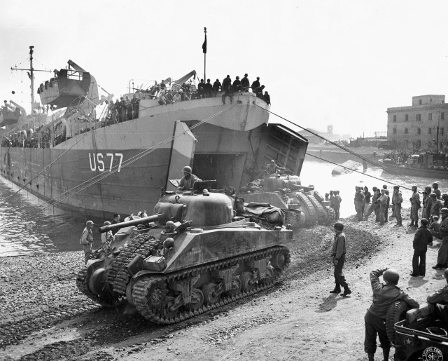 LST-77 off-loading M4 Sherman tanks at Anzio, Italy, May 1944; note the small barge capsized in the background