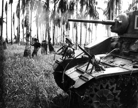 7 January 1943. Australian forces attack Japanese positions near Buna. Members of the 2/12th Infantry Battalion advance as Stuart tanks from the 2/6th Armoured Regiment attack Japanese pillboxes. An upward-firing machine gun on the tank sprays treetops to clear them of snipers. (Photographer: George Silk).