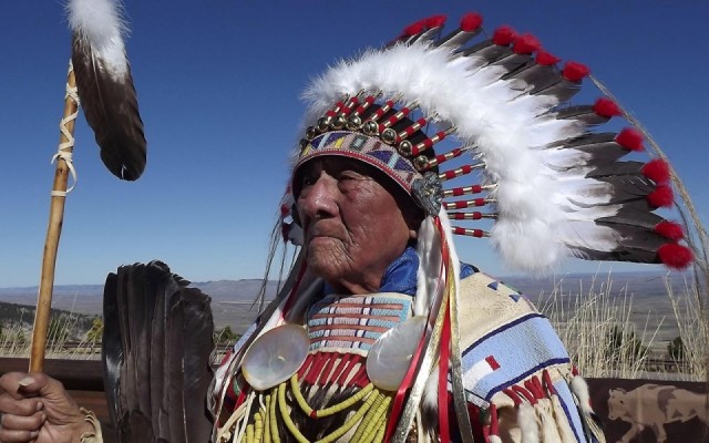 In this family photo, Joseph Medicine Crow wears a headdress beaded by his granddaughter and a war shirt from the Custer Battlefield Trading Post in Crow Agency, Montana. The Bighorn Mountains are in the background. 