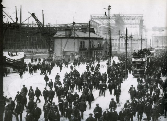 Harland and Wolff Workers leaving the shipyard at Queens Road in early 1911. RMS Titanic is in the background, beneath the Arrol gantry.