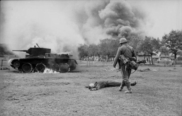 German soldier looking at corpse of Soviet soldier and destroyed tank BT-7 on steppes of Ukraine. 1941