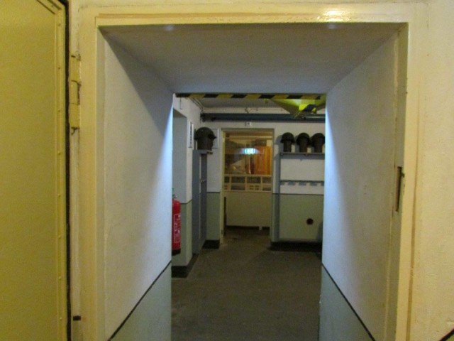 Walls with gun racks, gas mask cans, helmets and a furnished living room.