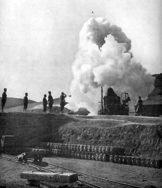 A Japanese 11 inch (275 mm) siege gun fires on Port Arthur during the Russo-Japanese war. The 500 pound (250 kg) shell can be seen in flight above the gun.