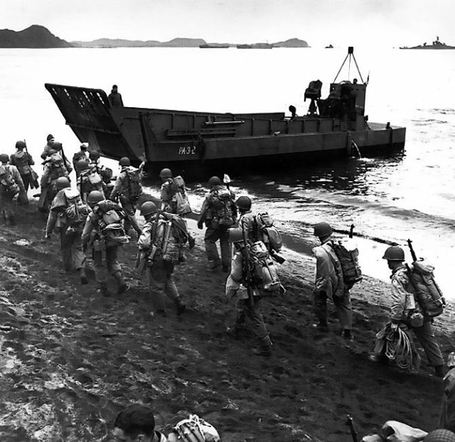 Troops march up the beach at Adak Island, during pre-invasion loading for the Kiska Operation, August 13, 1943. The LCM behind the soldiers is from USS Zeilin (APA-3). Note the troops’ packs and M1 rifles.