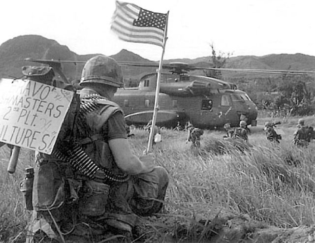 A Marine from 2nd Platoon "Vultures," of Bravo Company "Bushmasters," bares the Stars and Stripes while others from his unit board a CH-53A Sea Stallion with Marine Heavy Helicopter Squadron 463 in Vietnam in 1967.