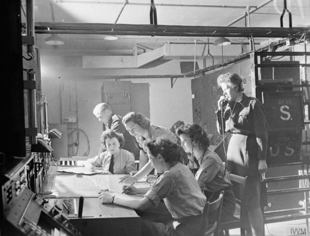 Flight Officer P M Wright supervises (right) as Sergeant K F Sperrin and WAAF operators Joan Lancaster, Elaine Miley, Gwen Arnold and Joyce Hollyoak work on the plotting map in the Receiver Room at Bawdsey CH, Suffolk. [© IWM (CH 15331)]